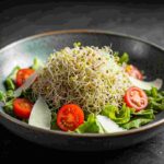 A bowl of sprouts salad with cherry tomatoes and lettuce.