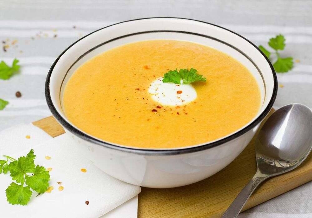 Dal Tadka Recipe: A bowl of creamy, yellow lentil soup garnished with yogurt, red chili flakes, and fresh parsley.