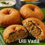 Four golden brown Ulli Vadas (onion fritters) on a green banana leaf, one cut in half showing the filling, with two small bowls of white and yellow chutneys in the background.