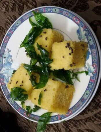 Khaman Dhokla Recipe: Fluffy Khaman Dhokla on a plate garnished with curry leaves and mustard seeds.