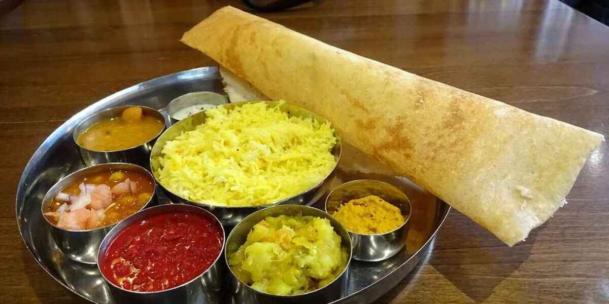 Masala Sambar Recipe: A delicious South Indian Thali meal featuring a crispy Masala Dosa (stuffed crepe) alongside bowls of vibrant Sambar, Rasam, coconut chutney, potato curry, tomato chutney, and a small portion of yellow rice on a round stainless steel platter.