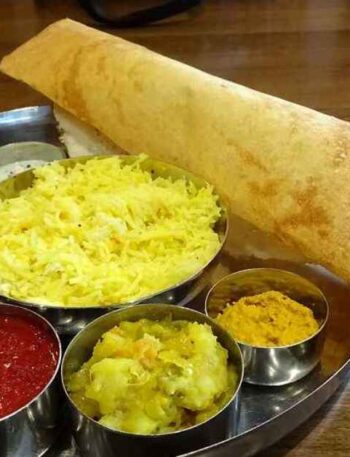 Masala Sambar Recipe: A delicious South Indian Thali meal featuring a crispy Masala Dosa (stuffed crepe) alongside bowls of vibrant Sambar, Rasam, coconut chutney, potato curry, tomato chutney, and a small portion of yellow rice on a round stainless steel platter.